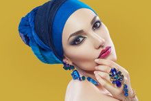 Beautiful Middle Eastern Woman With Hijab With Blue Scarf And Blue Jewelry And Red Lips On Yellow Background, Studio Shot. Looking At Camera.