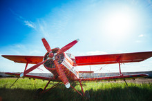 Red Retro Airplane Stands On Grass Against A Blue Sky With Flare