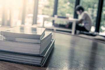 stack of books on wooden table on blur people read a book backgr