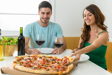 Boyfriend and girlfriend eating a large supreme pizza at home on a date with wine