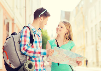 smiling couple with map and backpack in city