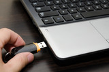 Fototapeta Miasta - hand with usb flash drive inserting it into laptop computer closeup
