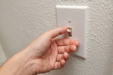 Hand turning wall light switch off. color image in horizontal orientation