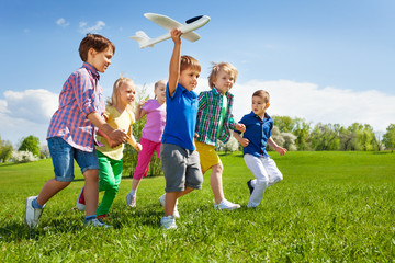 Boy with other kids runs and holds airplane toy