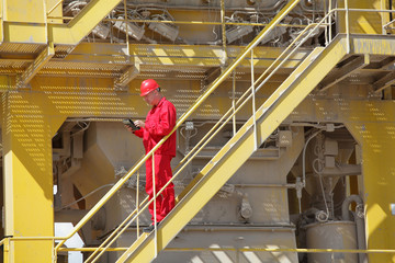 technician in coveralls and hardhat with tablet controlling industrial process