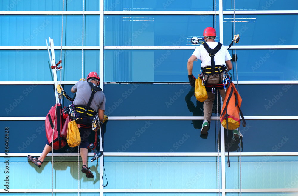 Two construction workers working at height on modern commercial skyscraper - obrazy, fototapety, plakaty 