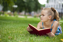 Adorable Cute Little Girl Reading Book Outside On Grass