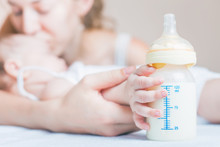 Baby Holding A Baby Bottle With Breast Milk For Breastfeeding. Mothers Breast Milk Is The Most Healthy Food For Newborn Baby.