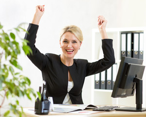 Successful middle-aged business woman with arms up sitting at pc in office