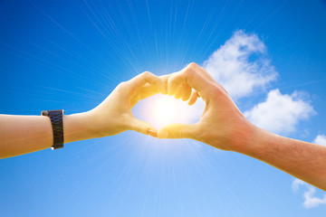 Couple making a finger heart in the sunny sky