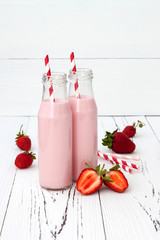 Strawberry milk in traditional glass bottles with straws on old vintage wooden background