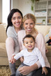 © dglimages - Female couple sit together with their son in their home and all smile for the camera