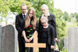 Familie steht in Trauer an Grab auf Friedhof bei Beerdigung
