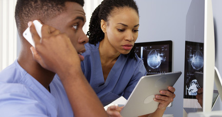 Two African American doctors using tablet and phone to work together