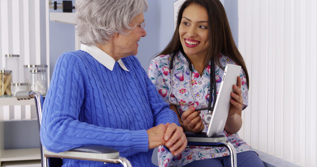 Friendly Mexican caregiver talking to elderly patient with tablet