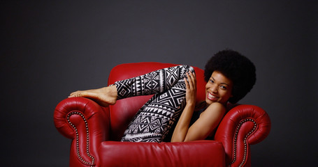 African woman in red leather arm chair kicking legs playfully