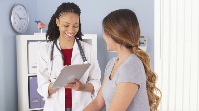 Wall Mural -  - Black doctor with tablet talking to female Asian patient