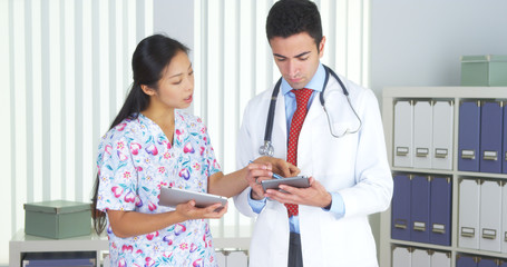 Wall Mural - Hispanic doctor talking with Asian nurse with tablets