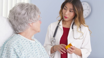 Wall Mural - Asian doctor talking to elderly woman in bed about prescription medication