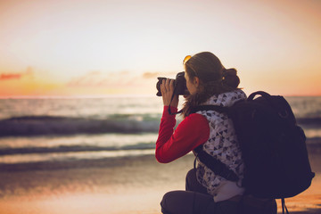 Girl photographer taking pictures with SLR camera at sunset on