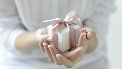 Wall Mural - Close up shot of female hands holding a small gift wrapped with pink ribbon. Small gift in the hands of a woman indoor. Shallow depth of field with focus on the little box.