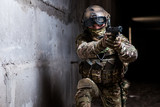Fototapeta Młodzieżowe - Armed ranger in camouflage aiming his gun in the dark room