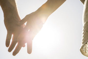 romantic couple with clasped hands backlit by a bright evening s