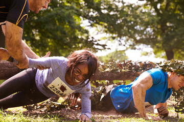 Assault course competitor helping others crawl under nets