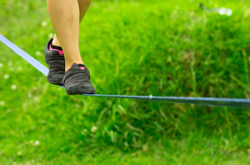 Closeup womans feet with shoes balancing on slackline and grassy background