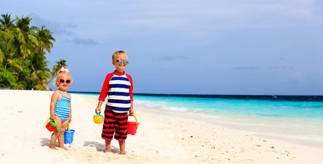 little boy and toddler girl play with sand on tropical beach