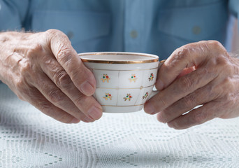  Senior man holding cup of tea in their hands at table close-up