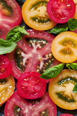 Cut pieces of colored tomatoes and basil leaves on a dark backgr