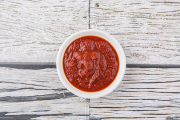 Fresh pureed tomato in white bowl over rustic wooden background