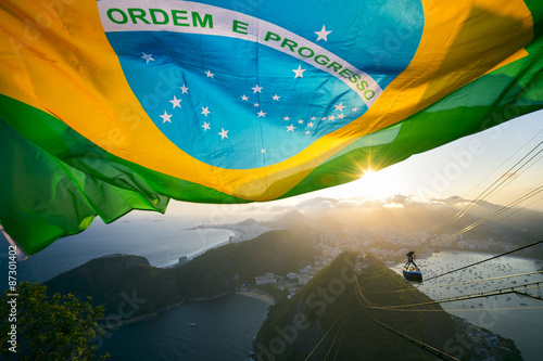 Photo Brazilian flag shines above the golden sunset city skyline at Sugarloaf Pao de A
