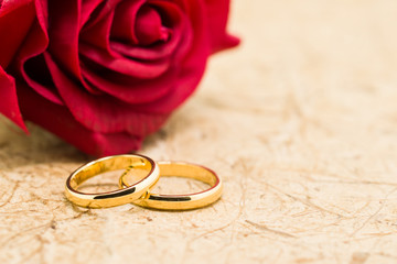 Wedding rings and artificial rose on brown background