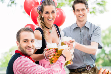 Wall Mural - Drei Freunde in Münchner Biergarten in Tracht stoßen mit Hellem an