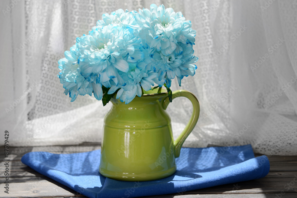 Beautiful chrysanthemums in pitcher on fabric background