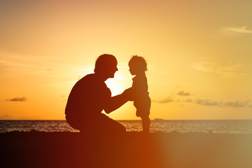 Wall Mural - Father and little daughter silhouettes holding hands at sunset