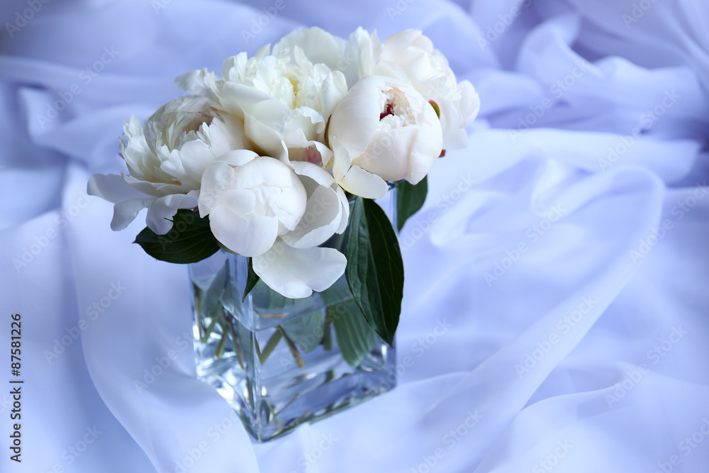 Beautiful white peonies in vase on fabric background