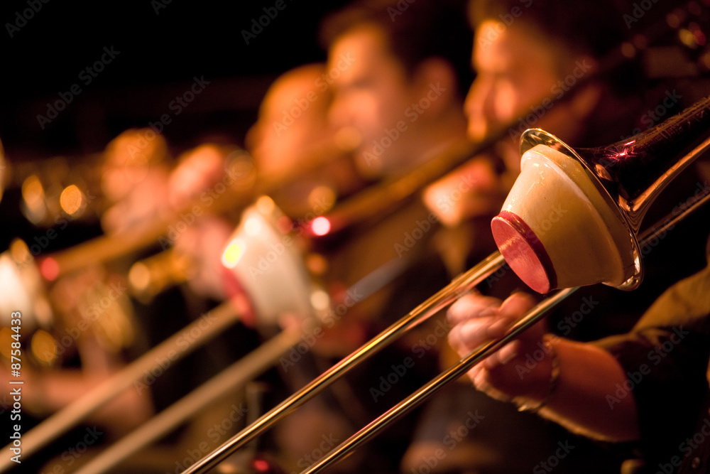 Jazz Big Band trombone section with cup mutes. Shallow focus on the foreground trombonist with the rest of the section falling into background blur. - obrazy, fototapety, plakaty 