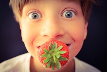 Wide Eyed Child With A Fresh Strawberry In His Mouth