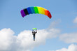 Parachutist on a bright  parachute  rainbow colors on bakcground blue sky with clouds