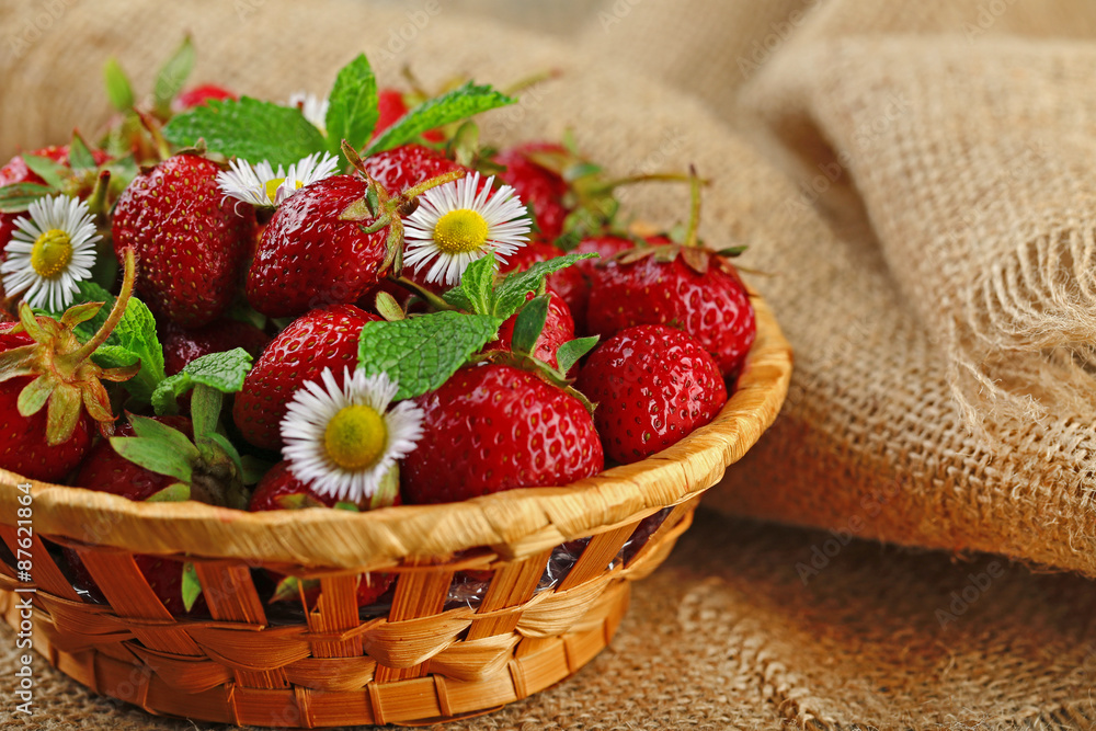 Red ripe strawberries in wicker basket, on wooden background