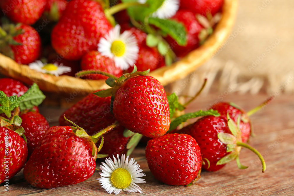 Red ripe strawberries in wicker basket, on wooden background