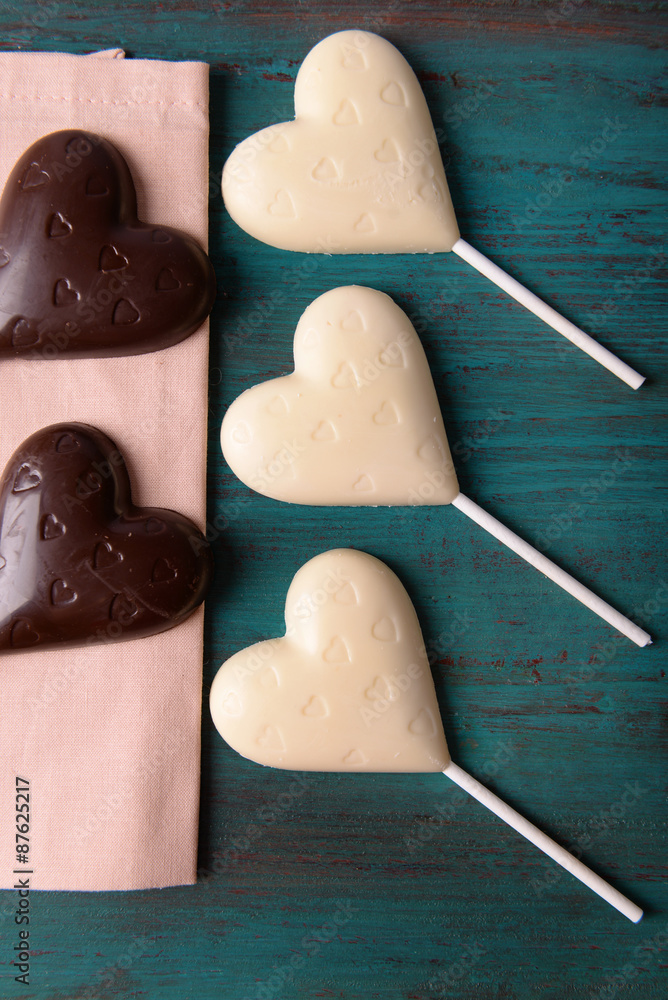 Chocolate heart shaped candies on sticks on wooden background