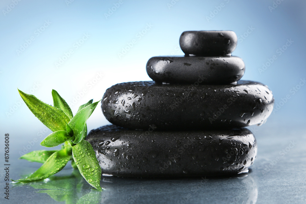 Stack of wet spa stones with green leaves on gray background