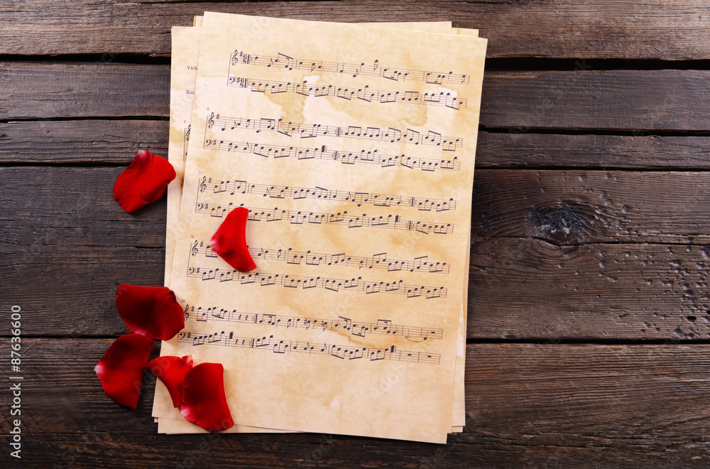 Beautiful rose petals on music sheets on wooden background
