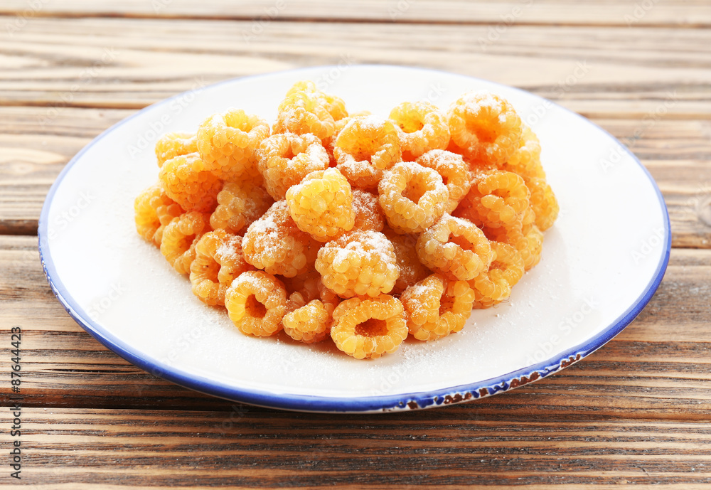 Yellow raspberries in white plate on wooden table, closeup