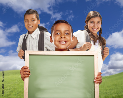 Hispanic Boys and Girl In Field Holding Blank Chalk Board
