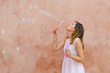 © creativefamily - Girl blowing soap bubbles against colourful backdrop